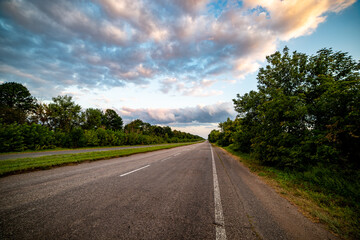 Fototapeta premium A picturesque asphalt road winds through lush green trees, inviting travelers into a serene natural landscape. Perfect for themes of adventure, travel, or nature exploration.