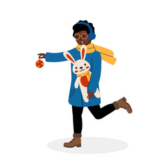 A joyful person holds a Christmas ornament while carrying a bunny plush on a winter day