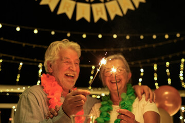 Happy family senior couple celebrating birthday at night party sparkling lights on home terrace - Two elderly people having fun together - Holidays lifestyle concept