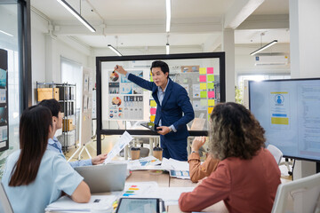 Obraz premium Group of young Asian professionals collaborating presentation project meeting in a modern office. Brainstorming innovative ideas for a new business venture.