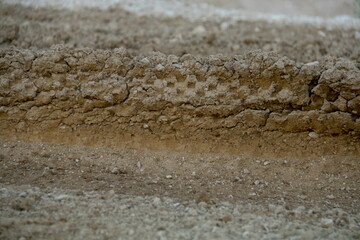 Huella de neumáticos de moto marcadas en la tierra compactada en el peralte de una curva, diferentes tonos de la arena, tierra, piedras acumuladas en el reborde agrietado