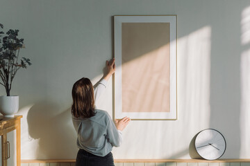 Rear view of a woman hanging a blank picture frame on a  wall in a living room