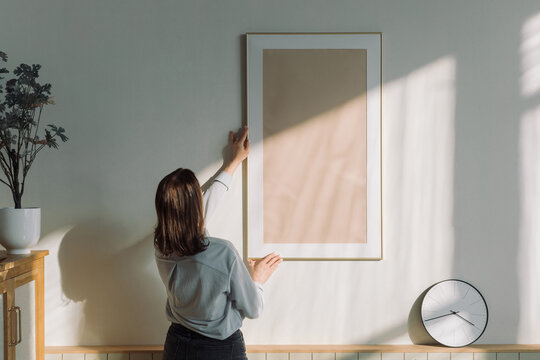 Rear view of a woman hanging a blank picture frame on a  wall in a living room