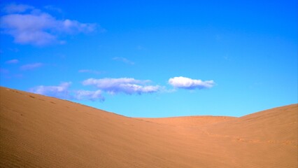The top of golden sand dunes with blue sky and isolated clouds in the background
