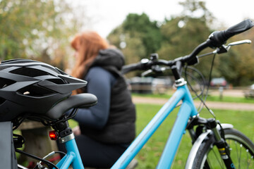 Female bicycle and helmet parked up while the hound rider has a coffee at a rural coffee shop. The young lady is seen resting on a park bench.