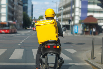 Delivery rider on a motorcycle navigating city streets during a bright sunny day in an urban...
