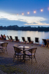 Relaxing evening by the waterfront with chairs, tables, and glowing lights near the calm water