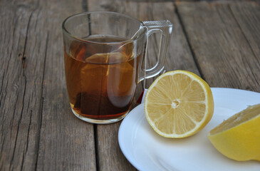 On a wooden table a glass mug with tea and lemon on a plate. selective focus. tea with lemon