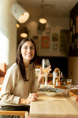 A joyful woman enjoying a glass of white wine while dining on a delicious meal at a trendy restaurant in the heart of the city
