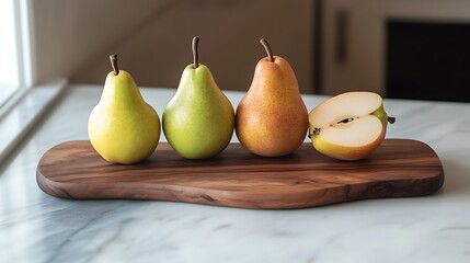 Four pears, two whole and one cut in half, arranged on a wooden cutting board on a white marble surface.