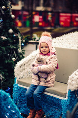 a five-year-old girl is on the street, there are New Year decorations around, she is dressed warmly