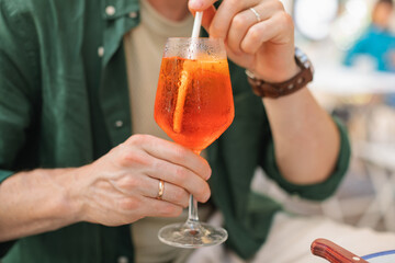 Close-up of a man sitting at an outdoor cafe drinking an orange spritz cocktail in summer