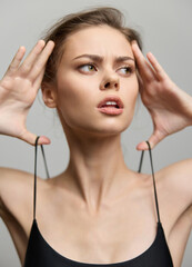 Fototapeta premium Stunning female model with a serious expression, wearing a black sleeveless top, showcasing contemporary fashion against a soft gray background.