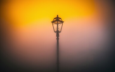 Obraz premium street lamp in the fog A single street lamp stands tall amidst a thick fog, bathed in warm sunset hues.