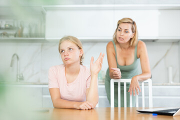 Mother and daughter are in conflict at home in kitchen. Annoyed mother is outraged by her daughters behavior and scolds yelling at teenager