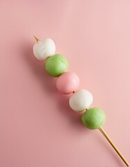 A skewer of mochi, a traditional Japanese dessert, in white, green, and pink, on a pink background.