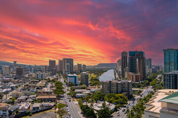 Fototapeta premium aerial shot of the Ala Wai Canal with skyscrapers, hotels and condos, lush green trees and cars driving on the street in Honolulu Hawaii USA