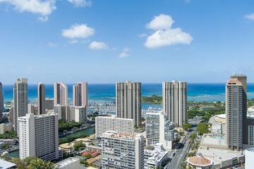 Naklejka premium aerial shot of the Ala Wai Canal with skyscrapers, hotels and condos, lush green trees and cars driving on the street, boats and yachts in the harbor in Honolulu Hawaii USA