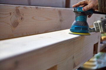 a man grinds wooden beams on the street with a hand sander 