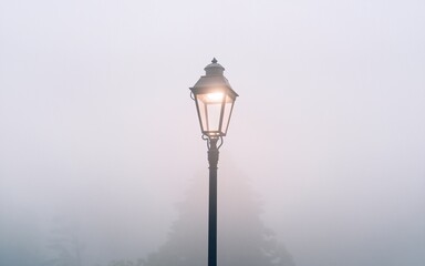 Fototapeta premium street lamp in the fog A single lamppost shines through a thick fog, casting a warm glow on the misty landscape.