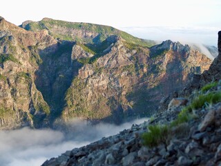 A breathtaking view of rugged mountain cliffs bathed in sunlight, enveloped in dense white fog, and...