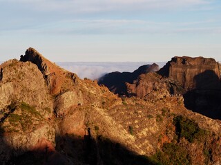 An awe-inspiring rocky ridge illuminated by the golden hour light, with a trail of hikers moving...