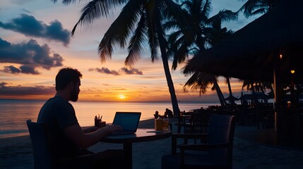 Man working on laptop at sunset on a tropical beach.