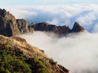 A stunning rock pinnacle dramatically emerges amidst a sea of thick fog, highlighted against a breathtaking cloudscape that invokes a sense of otherworldly magic - Pico do Arieiro, Madeira, Portugal.