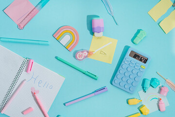 Notebook with word Hello made by kid near modern trendy bright school supplies on blue background