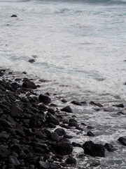 Coastline presents a rugged display of large rocks kissed by vibrant turquoise waves, creating a dynamic yet serene conjunction between earth and water elements - Madeira, Portugal.