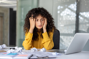 Young woman in office experiencing stress and frustration. Overwhelmed expression as she sits at...