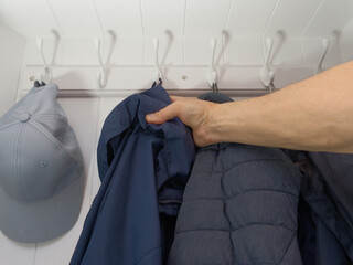 Closeup of a hand hanging a blue jacket on a white hook in a white cupboard, next to other casual clothing.