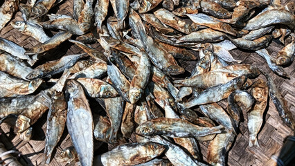 Salted fish being dried on a woven bamboo tray, showcasing texture and traditional details in food processing.