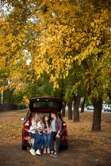Happy parents with daughter and cute dog Jack Russel terrier sitting in car trunk on autumn day. Long auto journey break.