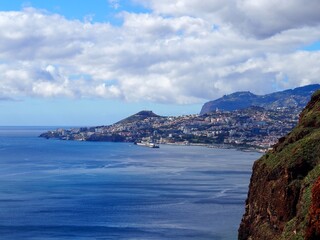 Fototapeta premium A breathtaking view of a coastal city nestled between the ocean and mountains, with clouds overhead, symbolizing harmony, grandeur, and nature magnificence - Madeira, Portugal.