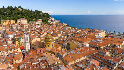 Aerial view of Nice, France, showcasing vibrant Mediterranean architecture with terracotta rooftops, historic churches, and the azure sea in the background. A picturesque coastal cityscape