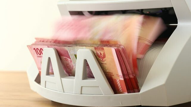 Indonesia money. Counting Indonesian banknotes of one hundred thousand rupiah using money converting machine. Financial concept. Currency exchange, bank calculations, business settlements