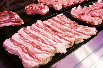 Raw pork and beef pieces of meat neatly cut and laid out behind the glass of the refrigerator on the counter in the supermarket