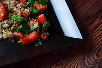 Salad with green leaves and vegetables. Lean vegetarian dish. Light salad organic mix lettuce with tomatoes, bulgur, parsley, seasoned roasted sesame seeds.