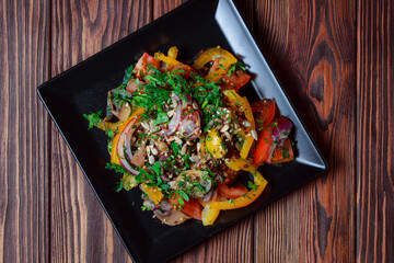 Salad of tomatoes and paper with fresh greens. On a brown wooden background. Fresh vegetable mix at dark table. Top view, Copy space.