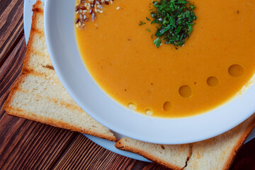 Vegetable soup with bread on wooden tray. White bowl on dark plank background. Top view. Copy space.