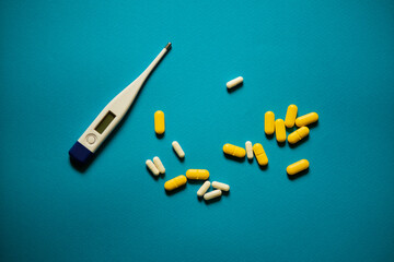 Various tablets and capsules alongside an electronic thermometer on a blue background.