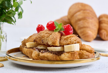 Croissant with banana pieces, chocolate paste in a round white plate