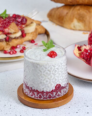 Glass with chia and yogurt dessert decorated with green mint leaf on white table