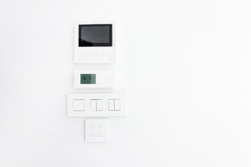Modern intercom display, air conditioning control, light switches and socket on white wall in apartment, free copy space