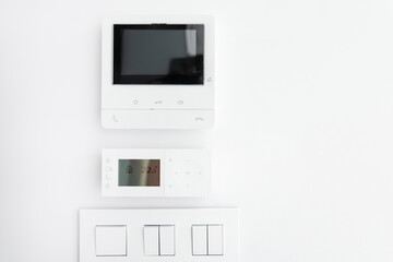 Empty display of modern intercom, air conditioning control panel and light switches on white wall, free copy space