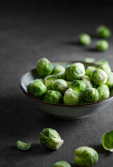 Raw brussels sprouts in a bowl on a dark background with fresh vegetables close up.