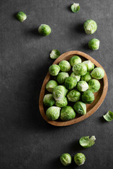 Fresh raw brussels sprouts in a wooden plate on a dark background.