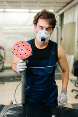 Vertical portrait of muscular expert car paint technician using car polisher to polish of car with refinement. Mechanic male using machinery car polishers maintenance to remove marks repair.