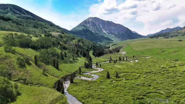 Aerial footage of an alpine meadow with a trout stream and mountains
